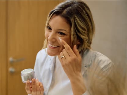 Anti-Aging-Creme mit Karotte Frau cremt sich vor Spiegel ein