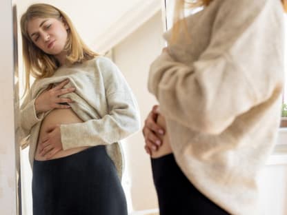 Blähbauch wegen Stress Frau schaut Bauch im Spiegel an