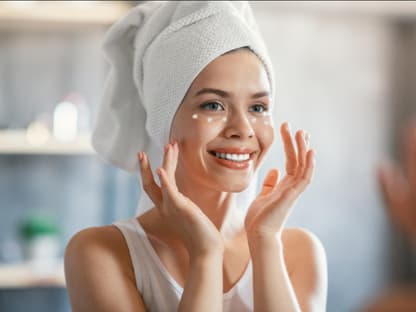 Anti-Aging-Creme für mehr Glow Frau strahlt in Spiegel, cremt sich ein