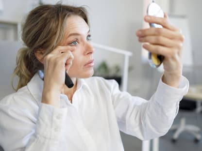 Frau mit Handspiegel schminkt wimpern