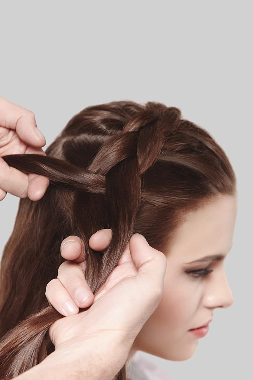Step 1: Eine etwa golfballgroße Menge Schaumfestiger (z. B. Pantene Pro-V Schaumfestiger Volumen Pur) in das noch feuchte Haar einkneten und auf niedriger Stufe trocken föhnen – das sorgt für Volumen und Textur. Dann das Haar auf Ohrhöhe abteilen, die komplette Partie am Oberkopf in drei Strähnen teilen und quer über den Oberkopf von einem Ohr zum anderen flechten.