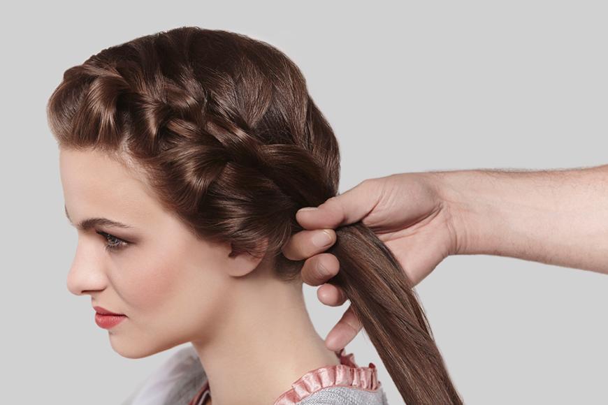 Step 2: Auf Ohrhöhe das Haar mit einem transparenten Haargummi fixieren, da ab hier die Flechttechnik vom Französischen zum Fischgratenzopf wechselt. Dazu das Haar in zwei gleich dicke Partien teilen. Nun eine dünne Strähne von der Außenseite der linken Partie abtrennen und zur Innenseite der rechten Partie führen.