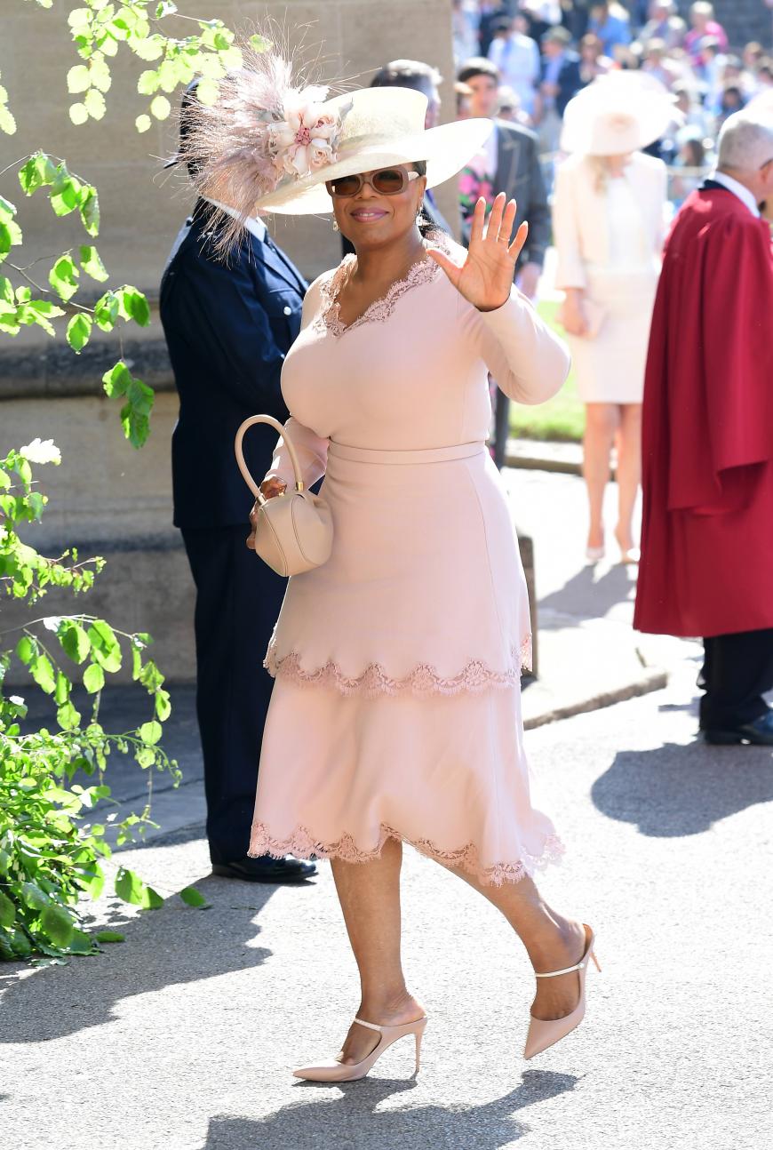 Talk-Masterin Oprah Winfrey winkt in einem zartrosafarbenen Kleid mit passendem Hut für die Kameras.
