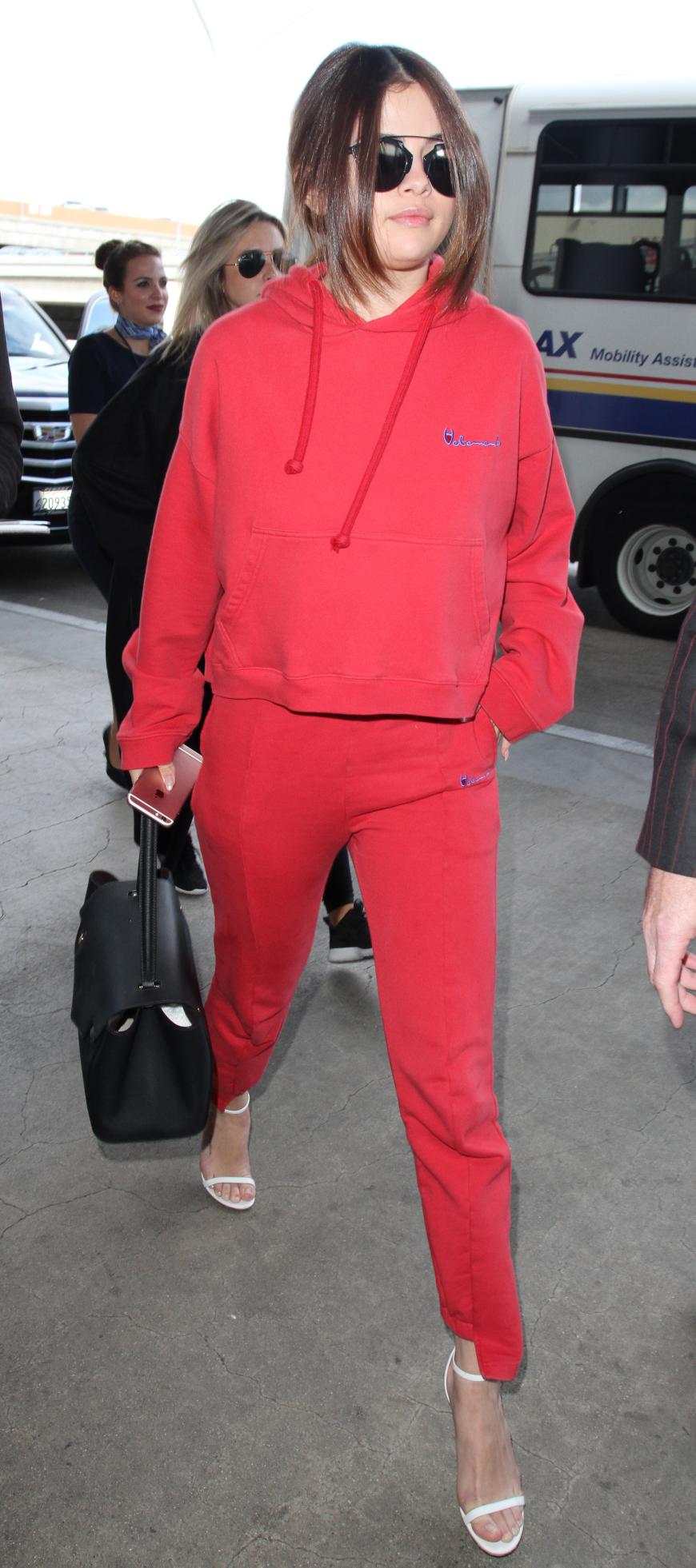 Selena Gomez reist bequem im roten Jogger - kombiniert dazu aber super sexy weiße Strap Heels!