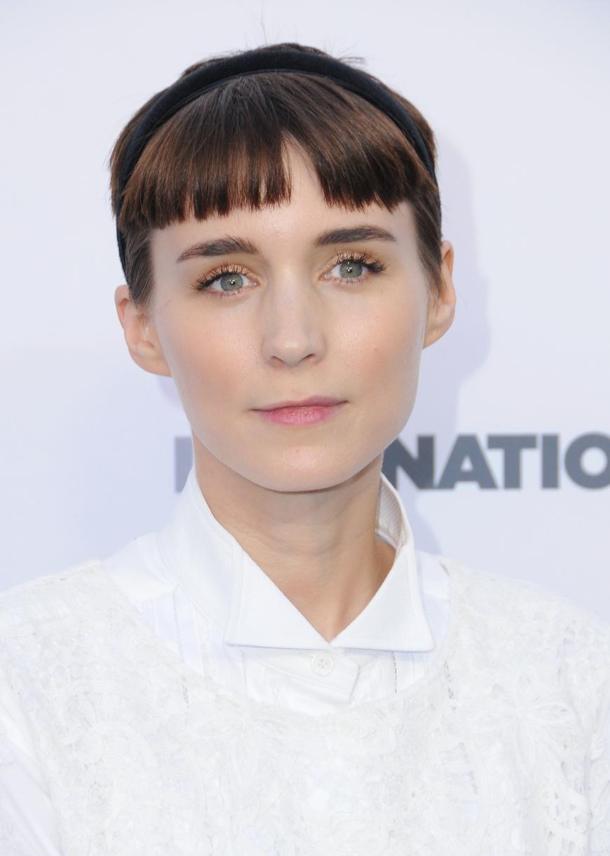 Bei Rooney Mara wirkt der Micro Pony fast etwas burschikos. Sie kombiniert die Trendfrisur zu einem schlichten Haarreif und weißer Bluse.