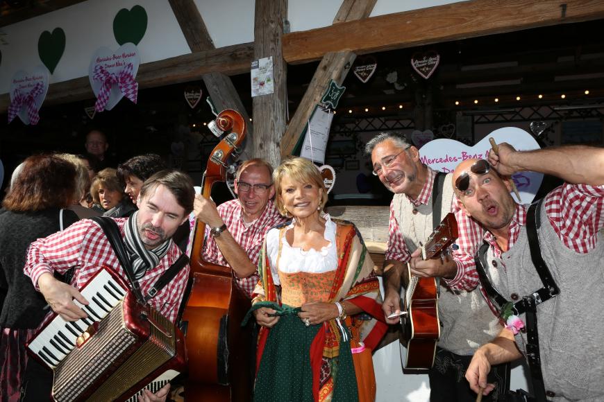 Schauspielerin Uschi Glas ist von fröhlichen Musikern umringt.