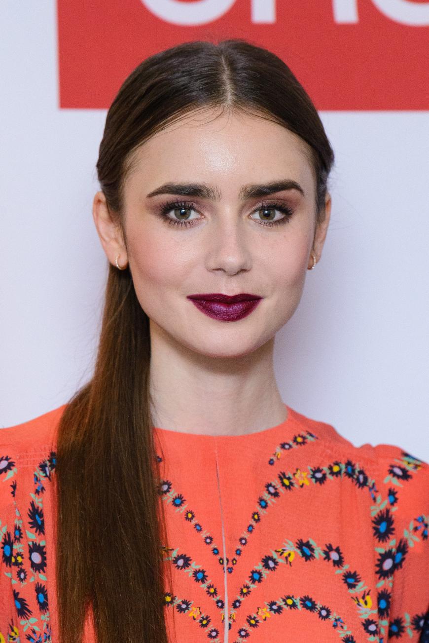 Lily Collins liebt Kontraste. Zu einem roten Kleid kombiniert sie lilafarbene Lippen.