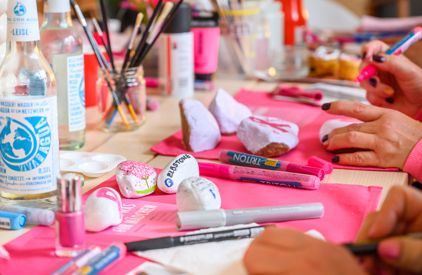 Ob mit Pinsel oder Stift — die kleinen Steine wurde mit feinen Motiven, wie der ikonischen Pink-Ribbon-Schleife, verziert, mit aufmunternden Worten versehen und in der Farbe Pink eingefärbt.