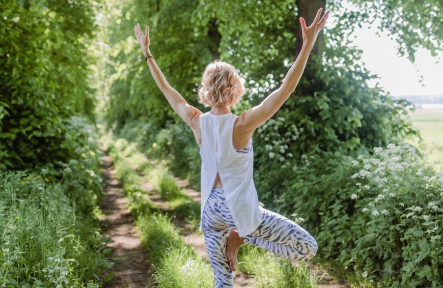Baum = Vrksasana: Verwurzel dich im Stehen vom Becken über die Beine in deine Füße, konzentriere dich auf einen Punkt vor dir, der sich nicht bewegt. Verlagere dein Gewicht auf deinen linken Fuß, dreh deinen rechten Fuß, das Knie und die Hüfte ein Stück nach außen rechts und zieh deinen Fuß an die Innenseite des linken Beins. Verneige das Knie dabei. Drück den Fuß sanft gegen das Bein und das Bein gegen den Fuß. Lege deine Hände vor deinem Brustbein aneinander, zentriere dich mit ein paar ruhigen Atemzügen.