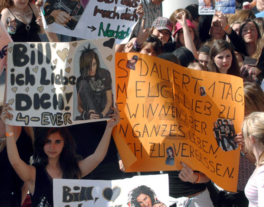 Fans warten vor einem Konzert und halten Plakate hoch