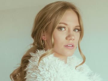 Blondine mit Pferdeschwanz trägt Teddy-Jacke und hat auffallende Wimpern