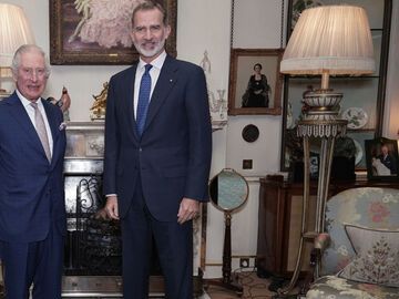 König Charles steht neben König Felipe und einem Bild von Prinz Georges Taufe