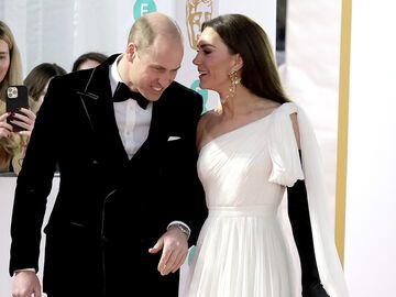 Prinzessin Kate flüstert Prinz William auf dem Roten-Teppich etwas zu. 