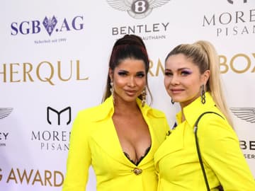 Micaela Schäfer und Yvonne Woelke stehen in abgestimmten gelben Outfits vor einer Fotowand und gucken in die Kamera