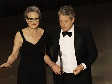 Andie MacDowell und Hugh Grant stehen vor einem Mikro auf der Bühne bei den Oscars 2023