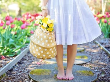 Frau steht barfuß im Blumenbeet