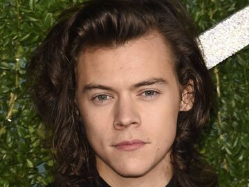 Harry Styles mit langen Haaren guckt ernst im Nadelstreifen-Anzug