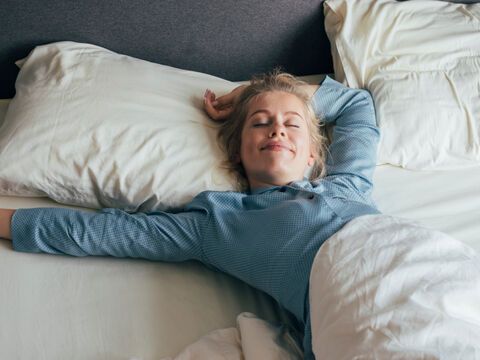 Blondine im blauen Pyjama streckt sich im weißen Bett