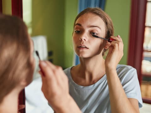 Frau trägt Mascara vor Spiegel auf