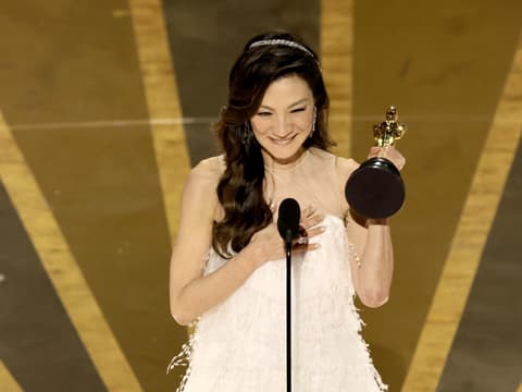 Michelle Yeoh mit Oscar-Trophäe in der Hand grinst vor Mikro auf der Bühne