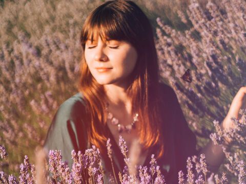 Frau mit geschlossenen Augen lächelt entspannt auf dem Lavendelfeld