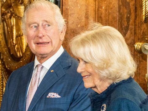 König Charles III. guckt nach oben, neben ihm steht Queen Consort Camilla, die lacht