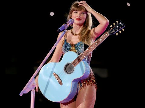 Taylor Swift mit Gitarre um den Bauch lächelt und fährt sich durch die Haare