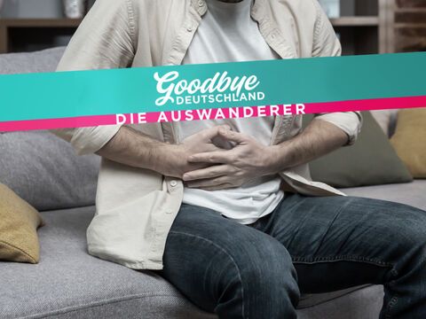 Mann hält sich den Bauch vor Schmerzen, davor das "Goodbye Deutschland"-Logo