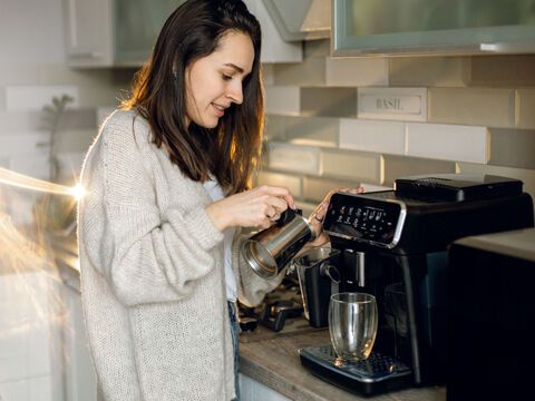 Frau bereitet am Vollautomaten einen Kaffee zu