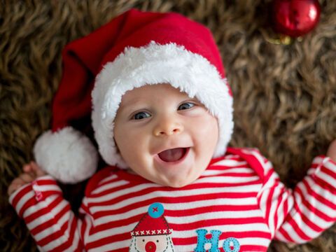 Lachendes Baby mit Weihnachtspullove rund Nikolausmütze