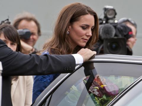 Prinzessin Kate steigt in ein Auto, ein Sicherheitsmann hält ihr die Tür auf. Im Hintergrund haben sich Paparazzi versammelt.