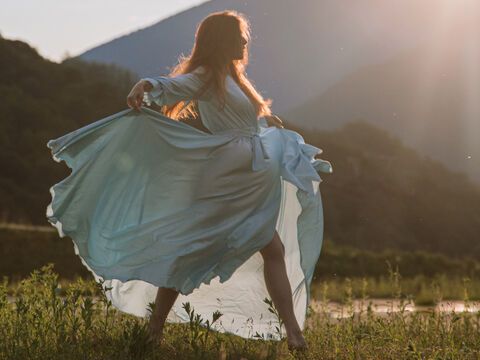 Frau tanzt in einem Kleid über eine Wiese mit Bergen im Hintergrund