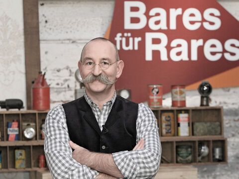  Horst Lichter mit verschränkten Armen vor dem "Bares für Rares"-Logo