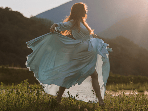 Frau tanzt in Kleid über Wiese