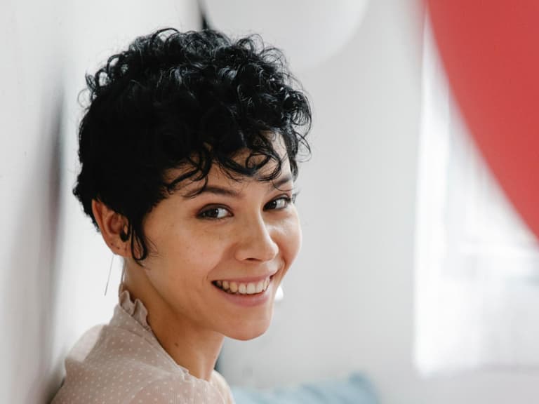 Frau mit kurzen, schwarzen Haaren hat Locken und lächelt in die Kamera.