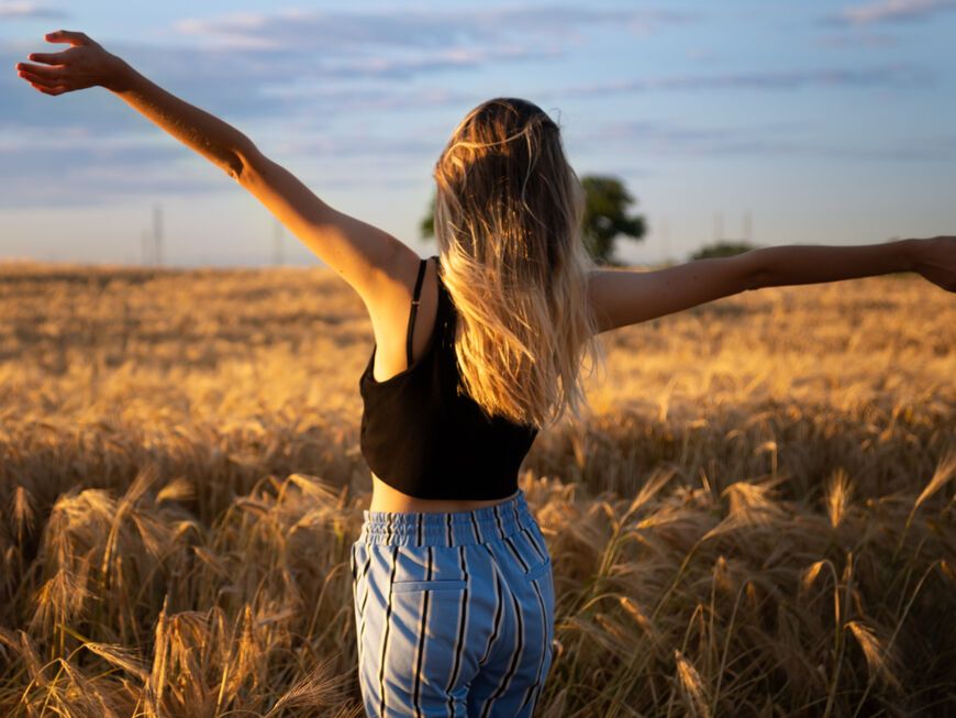 Frau steht mit offenen Armen im Getreidefeld.
