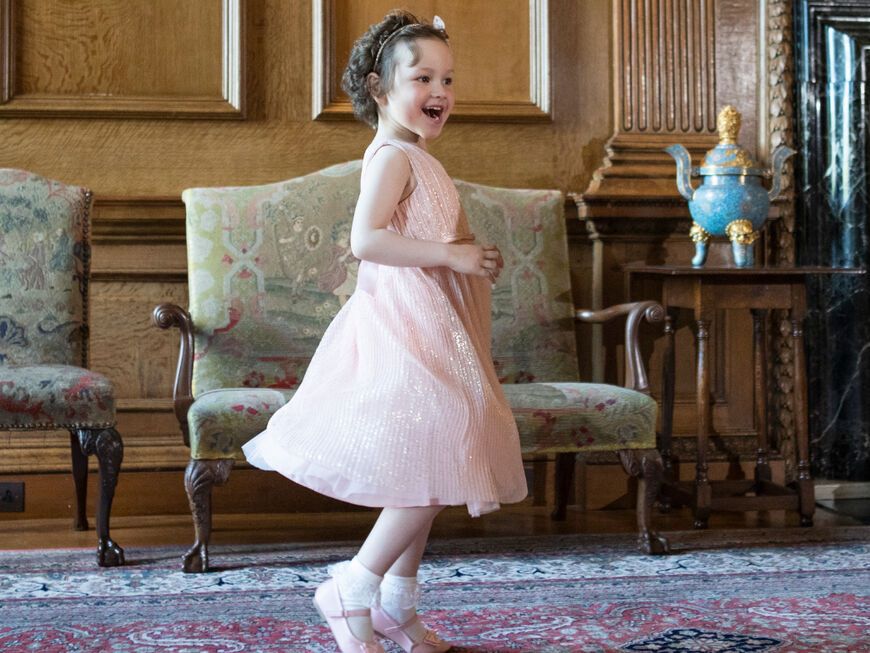 Mila Sneddon in rosa Kleid hüpft lachend