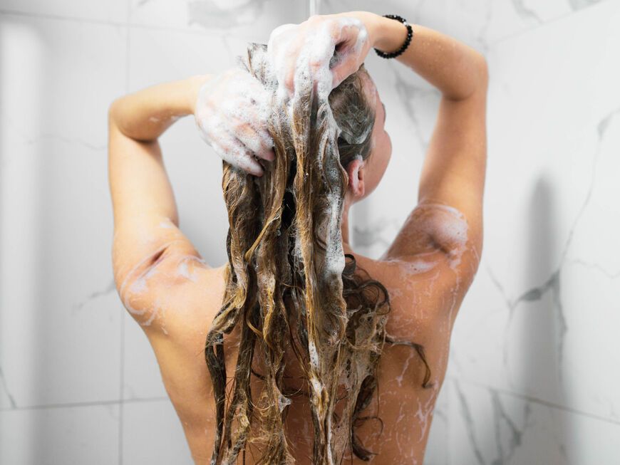 Frau von hinten wäscht sich die Haare in der Dusche
