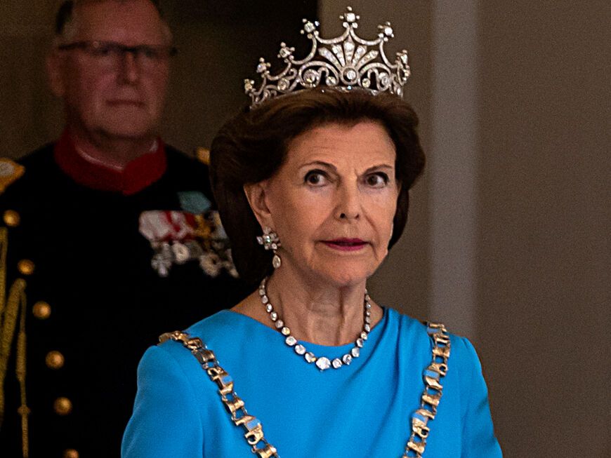 Königin Silvia von Schweden im königlichen Kostüm guckt konzentriert an der Kamera vorbei.