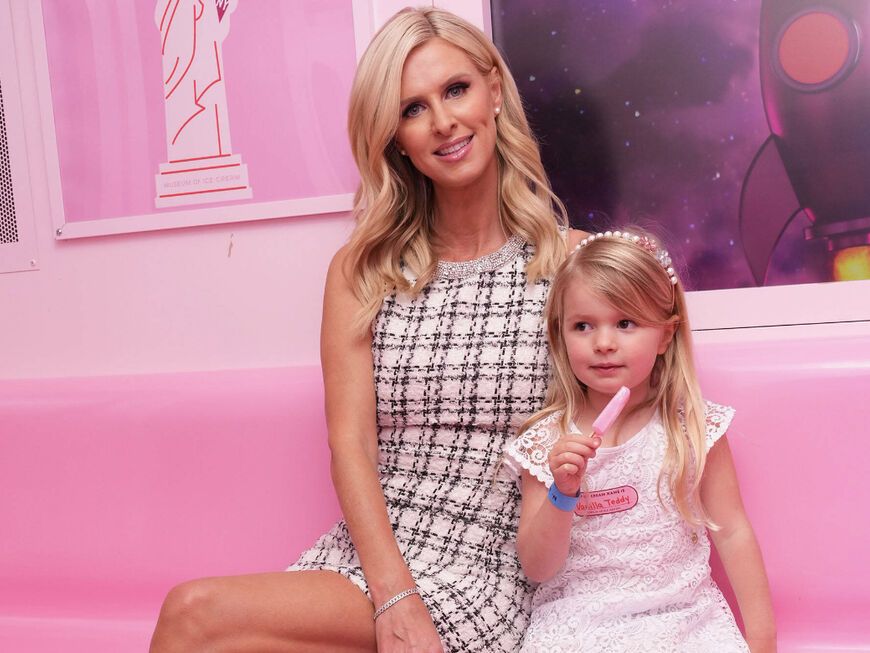 Nicky Hilton sitzt mit Tochter Teddy auf einer rosa Bank und isst Eis.