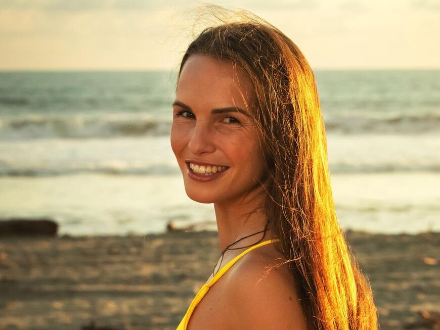 Bachelor 2023 Kandidatin Lisa M. steht am Strand und strahlt über die Schulter in die Kamera