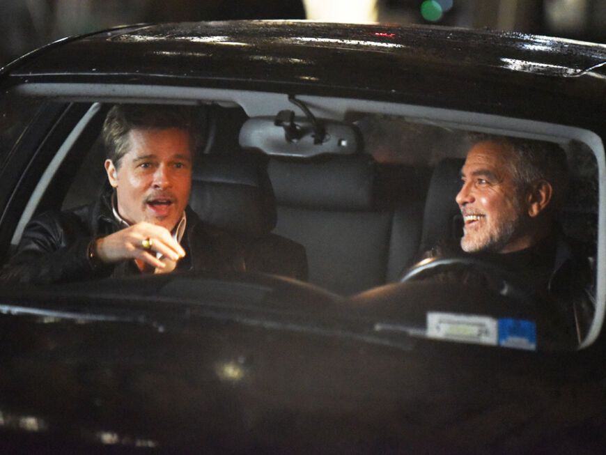 George Clooney und Brad Pitt lachen im Auto am Filmset von Wolves