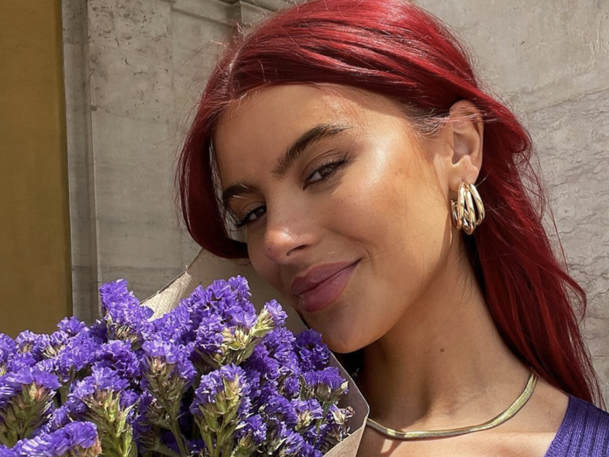 Romina Palm lächelt mit einem Strauß lila Blumen vor der Brust