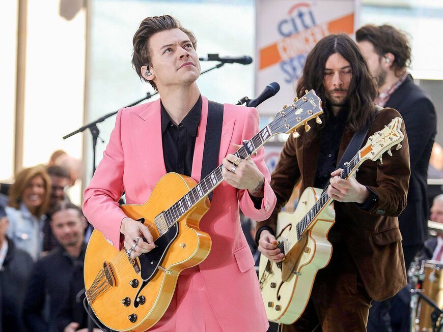 Harry Styles mit Gitarre in der Hand und pinken Anzug guckt hoch