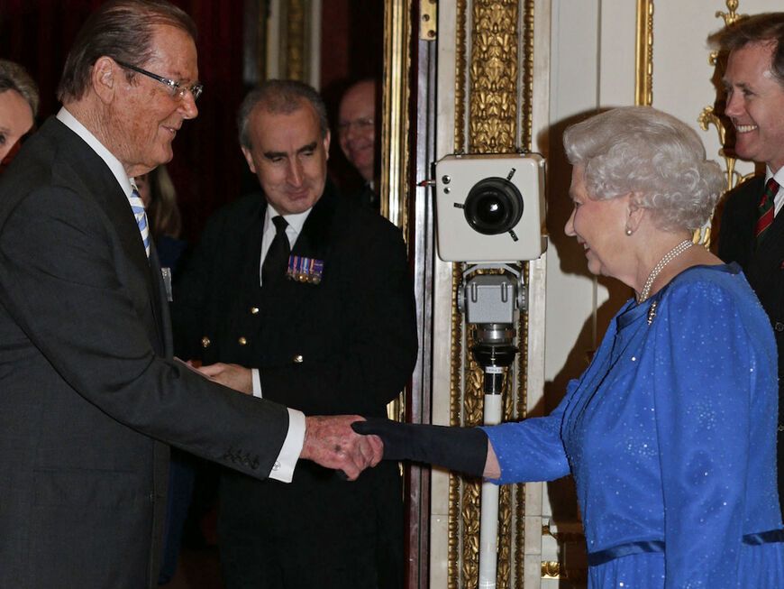 Roger Moore und Queen Elizabeth II. schütteln Hände