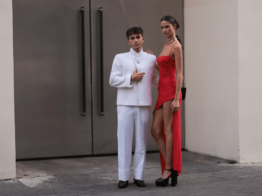 Julien Brown im weißen Anzug und Angelina Frerk im roten Kleid stehen vor einer Tür