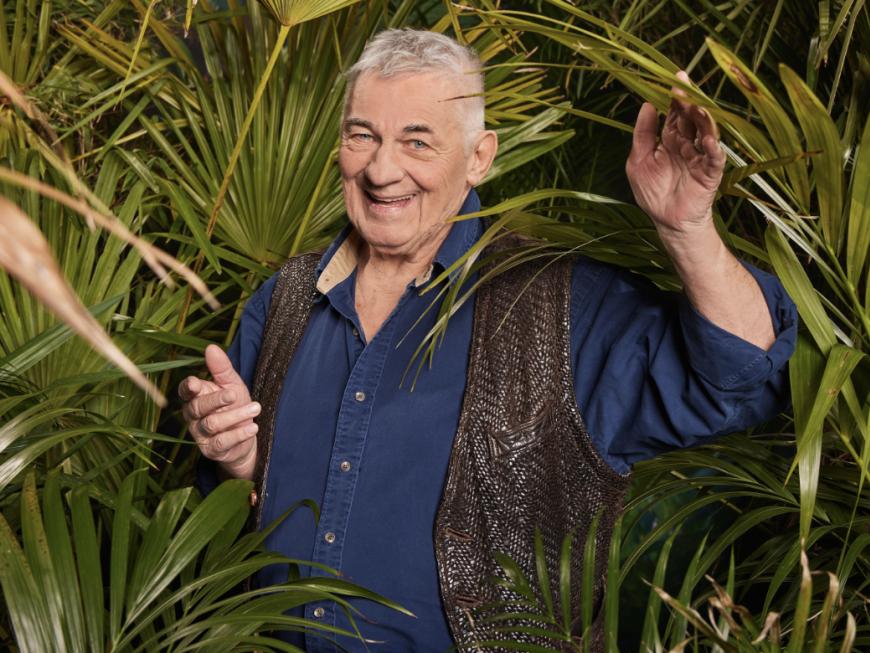 Heinz Hoenig lacht und winkt im Porträt für das Dschungelcamp 2024 im Gebüsch