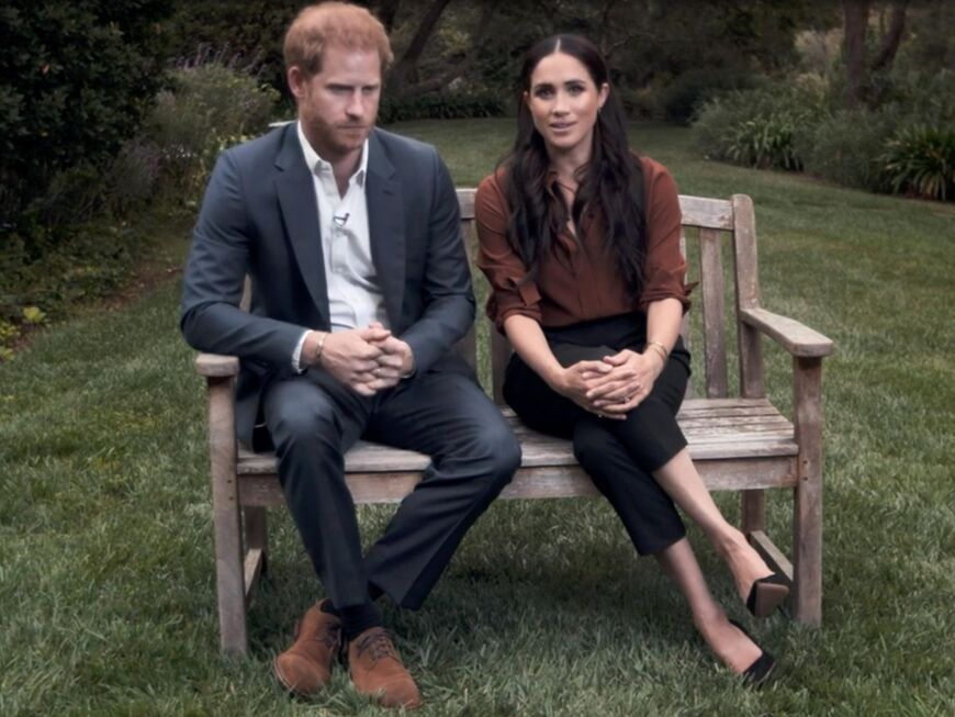 Prinz Harry und Herzogin Meghan sitzen gemeinsam auf einer Bank, schauen ernst