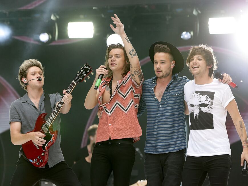 One Direction singen auf der Bühne, Niall Horan hält eine Gitarre in der Hand, Harry Styles ein Mikro