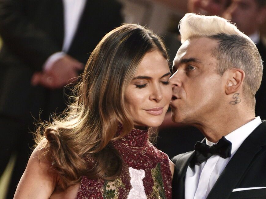 Robbie Williams küsst seine Ehefrau Ayda Field auf die Wange.